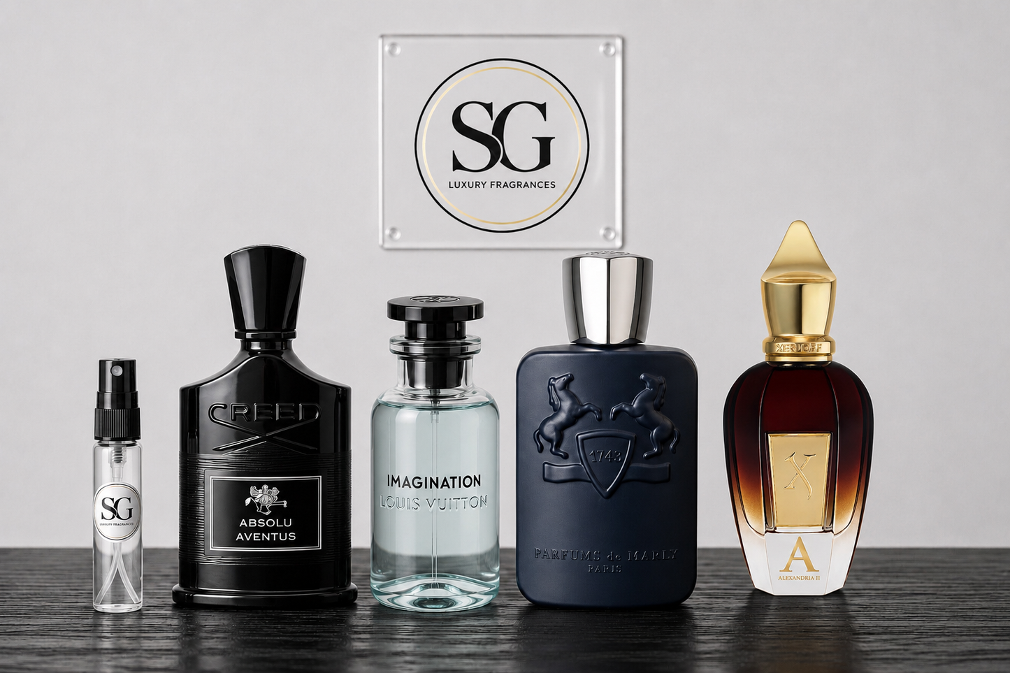 Five luxury perfume bottles arranged on a dark wooden surface against a light gray background, with a square 'SG Luxury Fragrances' sign centered above them. The bottles include a small clear spray vial, a black bottle labeled Absolu Aventus, a clear bottle labeled Imagination, a dark navy bottle with an embossed crest, and a brown-to-gold gradient bottle with a gold cap.