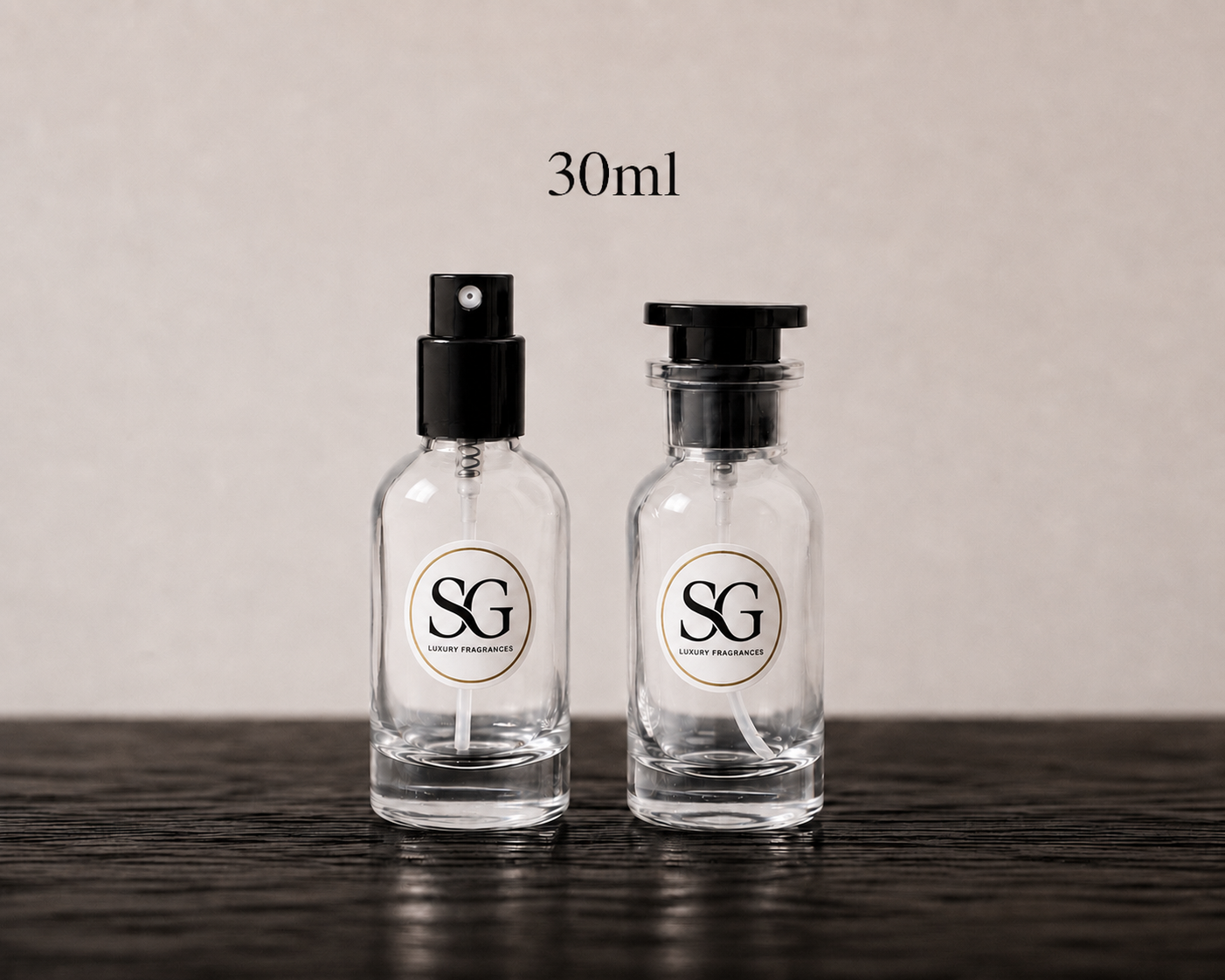 Two clear 30ml glass perfume bottles with black spray and cap tops, featuring a white circular label with the 'SG' logo, displayed on a dark wooden surface against a neutral beige background.