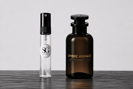 A Louis Vuitton Ombre Nomade perfume bottle in dark amber glass next to a small clear glass sample spray vial with a black atomizer and a silver circular label reading SG, set on a dark wooden surface against a light gray background.