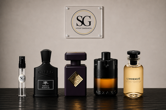Five luxury fragrance bottles from SG and Azaro arranged on a dark wooden surface against a beige wall, with an SG Luxury Fragrances sign hanging above.