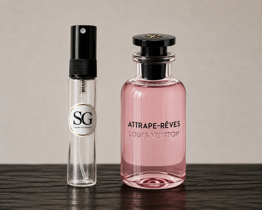 A clear glass perfume sample spray vial with a black spray top and a circular 'SG' label stands next to a larger pink Louis Vuitton 'Attrape-Rèves' perfume bottle, both placed on a dark wooden surface against a neutral beige background.