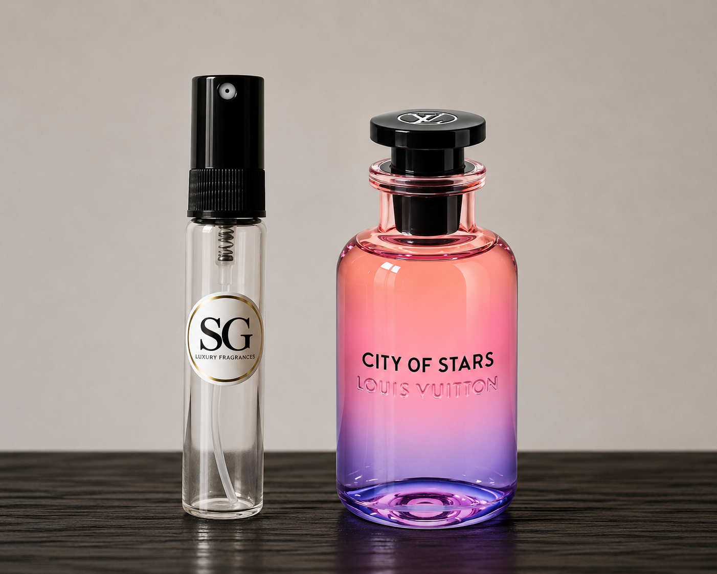 A small clear perfume atomizer spray bottle with a black spray top and a circular silver-and-black 'SG' label stands beside a larger Louis Vuitton 'City of Stars' perfume bottle with a pink-to-purple gradient glass body and black cap, set on a dark wooden surface against a plain light gray background.