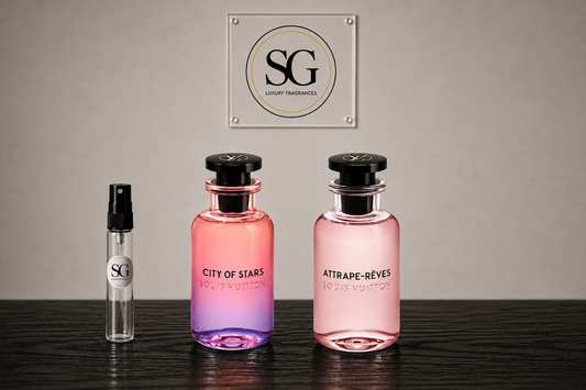Two perfume bottles and a small sample spray vial from SG Luxury Fragrances displayed on a dark wooden surface against a neutral gray wall. The bottles contain pink and purple gradient liquid, with 'City of Stars' and 'Attrape-Rèves' printed on the front.