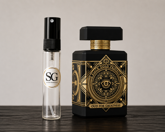 Black and gold perfume bottle with smaller clear bottle labeled 'SG' on a wooden surface.